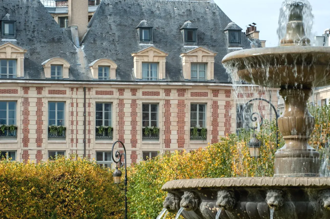 Fontaine devant un grand bâtiment Cour des Vosges Evok Collection à Paris