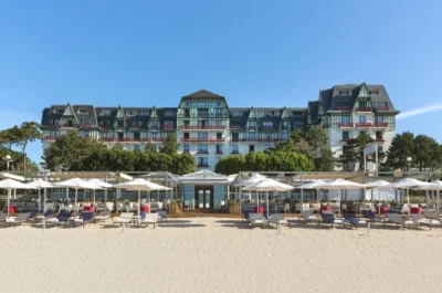 Plage avec des chaises et des parasols et un bâtiment davant Hôtel Barrière L'Hermitage à La Baule