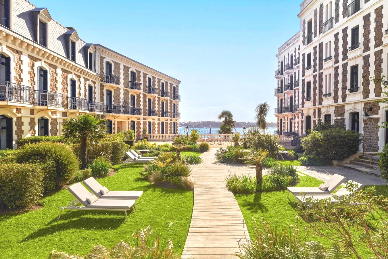 Rangée de bâtiments avec des bancs sur une promenade la mer en arrière-plan Hôtel Barrière Le Grand Hôtel Dinard